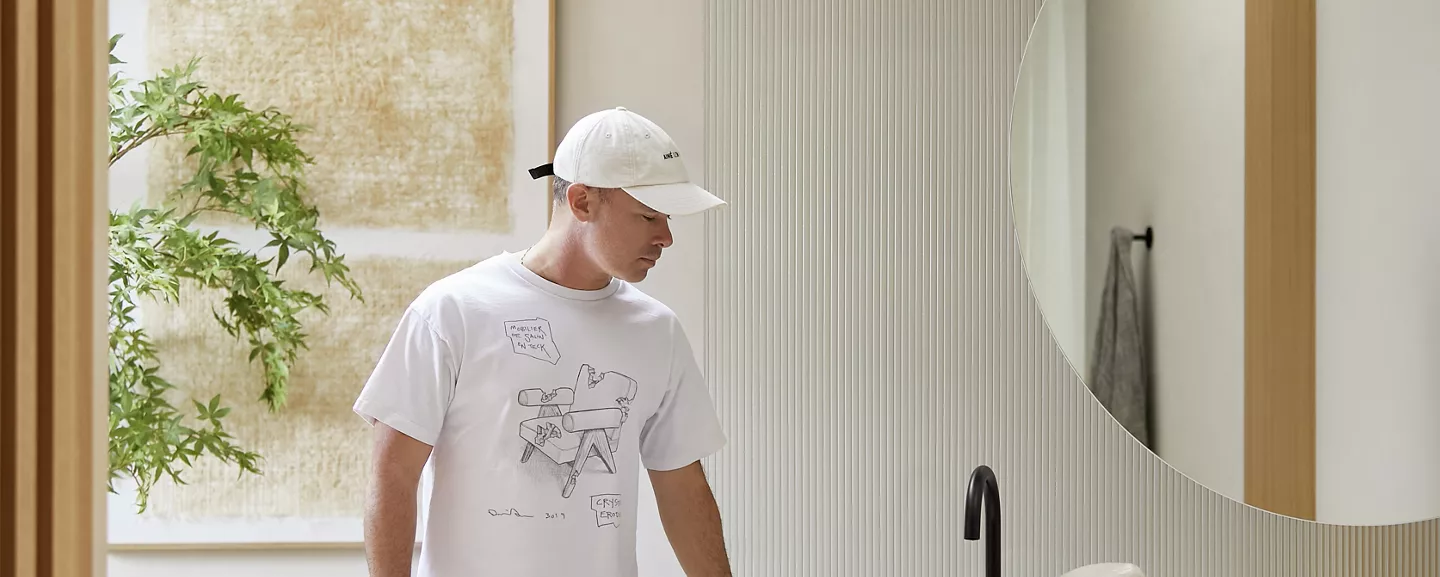 Daniel Arsham standing in a bathroom with his hand on the countertop as he looks down at the Rock.01 sink.